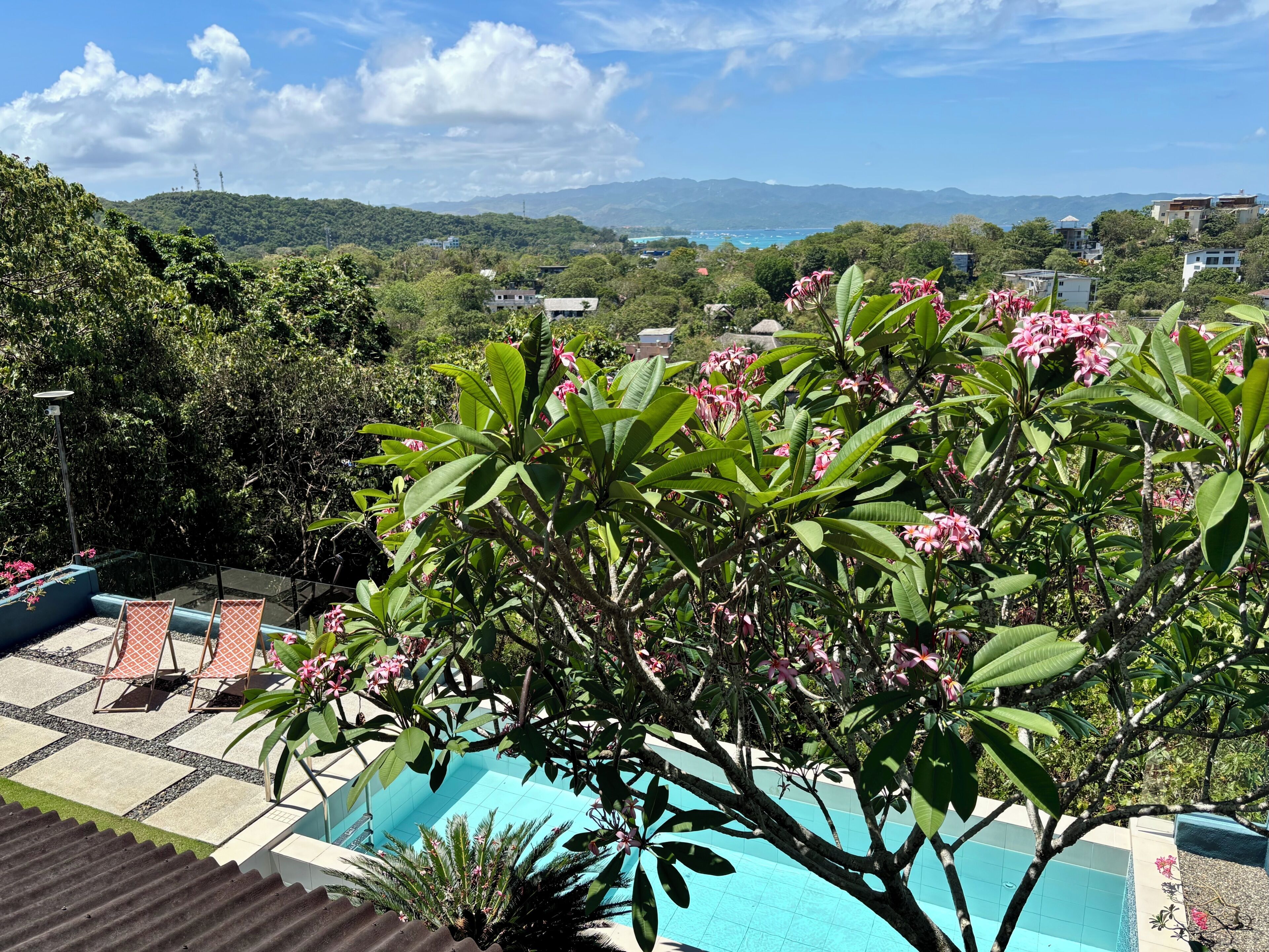 A pool area with a view of a mountainous landscape, surrounded by lush greenery and flowering plants.