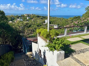 A residential area with a view of the ocean, a white building with a balcony, and a pathway leading to a gate.