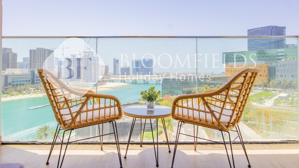 Un balcone con sedie in vimini e un tavolino, con vista su una città e un corpo d'acqua.