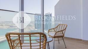 A balcony with wicker chairs and a table, overlooking a cityscape and water.
