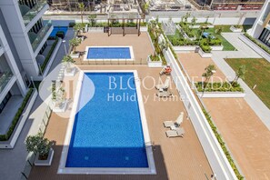 A rooftop pool area with two pools, surrounded by lounge chairs and planters.