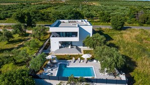 Una casa moderna de dos pisos con piscina, rodeada de abundante vegetación y un cielo despejado.