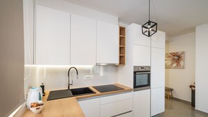 Una cocina moderna con armarios blancos, encimera de madera, horno integrado y una lámpara colgante negra.