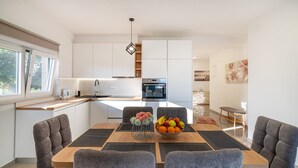 Una cocina moderna con armarios blancos, una isla central y una zona de comedor con sillas tapizadas en gris y una mesa de madera.