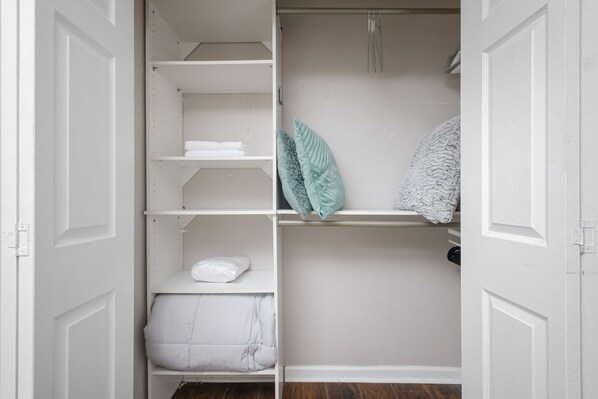 Een witte kast met planken, een kledingroede en een opgevouwen plaid.
