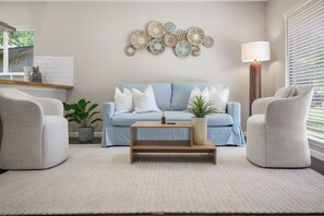 Un salon avec un canapé bleu clair, deux fauteuils, une table basse et un élément décoratif fixé au mur.