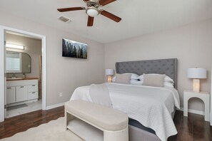 Une chambre à coucher comprenant un lit, des lampes de chevet, un ventilateur de plafond, un banc, une table de chevet, un miroir et un tableau accroché au mur.