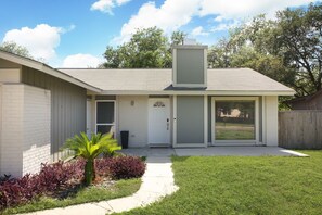 Une maison de plain-pied avec une porte d’entrée, un petit jardin devant la maison agrémenté d’un palmier, et une porte de garage.