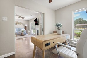A modern room with a wooden desk, a white chair, a ceiling fan, and a TV mounted on the wall. - Poolside Oasis near Sea World and Medical Center (Leon Valley)