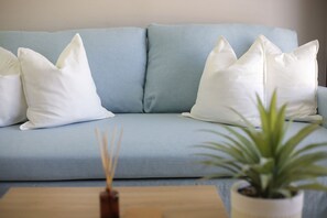 Een lichtblauwe bank met witte kussens en een kleine plant in een pot op een houten tafel.