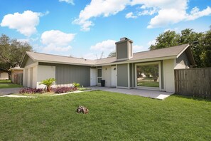 Une maison de plain-pied avec un porche à l’avant, un garage et un jardin à l’arrière, comprenant une pelouse et un petit palmier.
