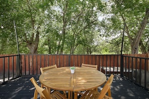 Une table ronde en bois, entourée de chaises, est délimitée par une clôture en bois et se trouve dans un espace extérieur ombragé, avec des arbres en arrière-plan.