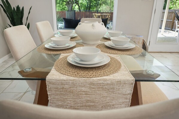 A dining table with white ceramic bowls and a white ceramic pot, surrounded by beige chairs.