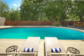 Une piscine avec deux chaises longues et une table, entourée d’une clôture en bois et d’arbres.