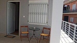 Un balcón con barandilla blanca, una ventana con rejas y dos sillas de madera con cojines.