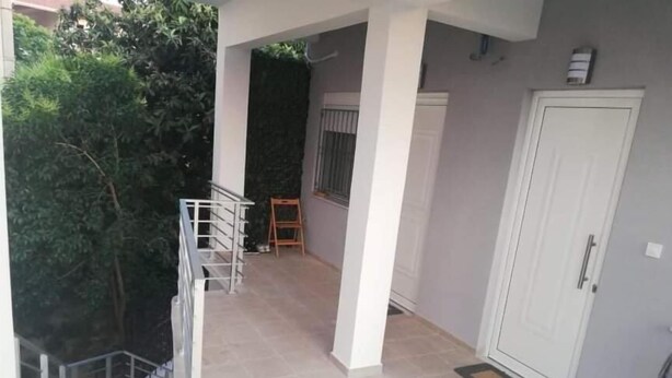 Un espacio al aire libre cubierto con una escalera que lleva a un nivel superior, una puerta blanca y una ventana con barandilla de metal.