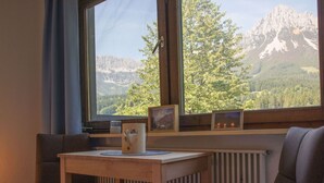 A cozy room with a wooden table and two chairs, a window with a mountain view, and a radiator below.