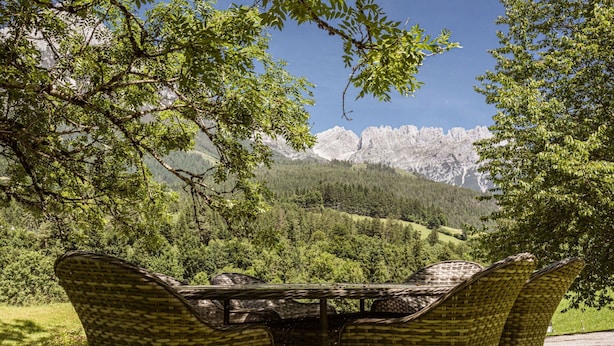 Een set rieten tafel en stoelen buiten, met uitzicht op een bergachtig landschap.