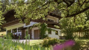 Een gebouw met twee verdiepingen en een balkon, omringd door weelderige begroeiing en bomen.