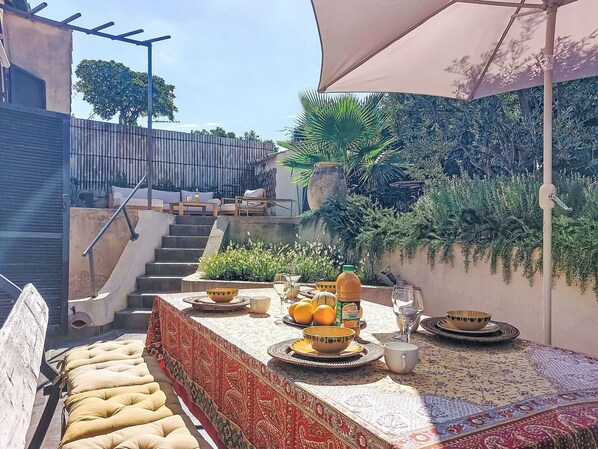 An outdoor dining area with a table set for two, surrounded by a garden and a staircase.