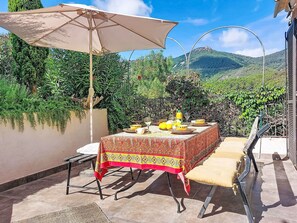 An outdoor patio with a table set for dining, surrounded by greenery and a mountain view.