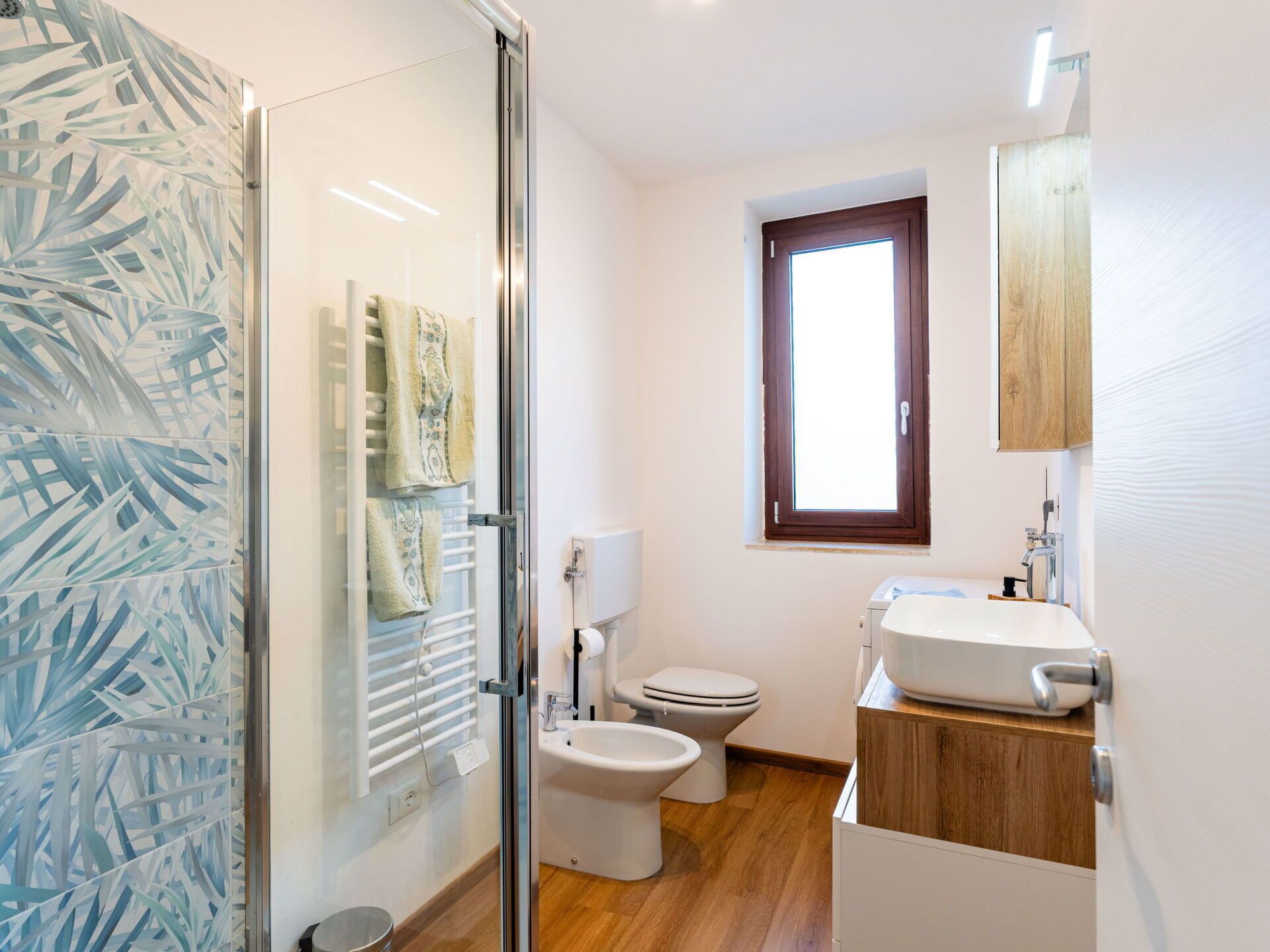 Un baño moderno con cabina de ducha de vidrio, inodoro, bidé y lavabo con mueble de tocador de madera.