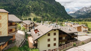 A mountain village with traditional chalet-style buildings, a cobblestone street, and a backdrop of forested mountains.