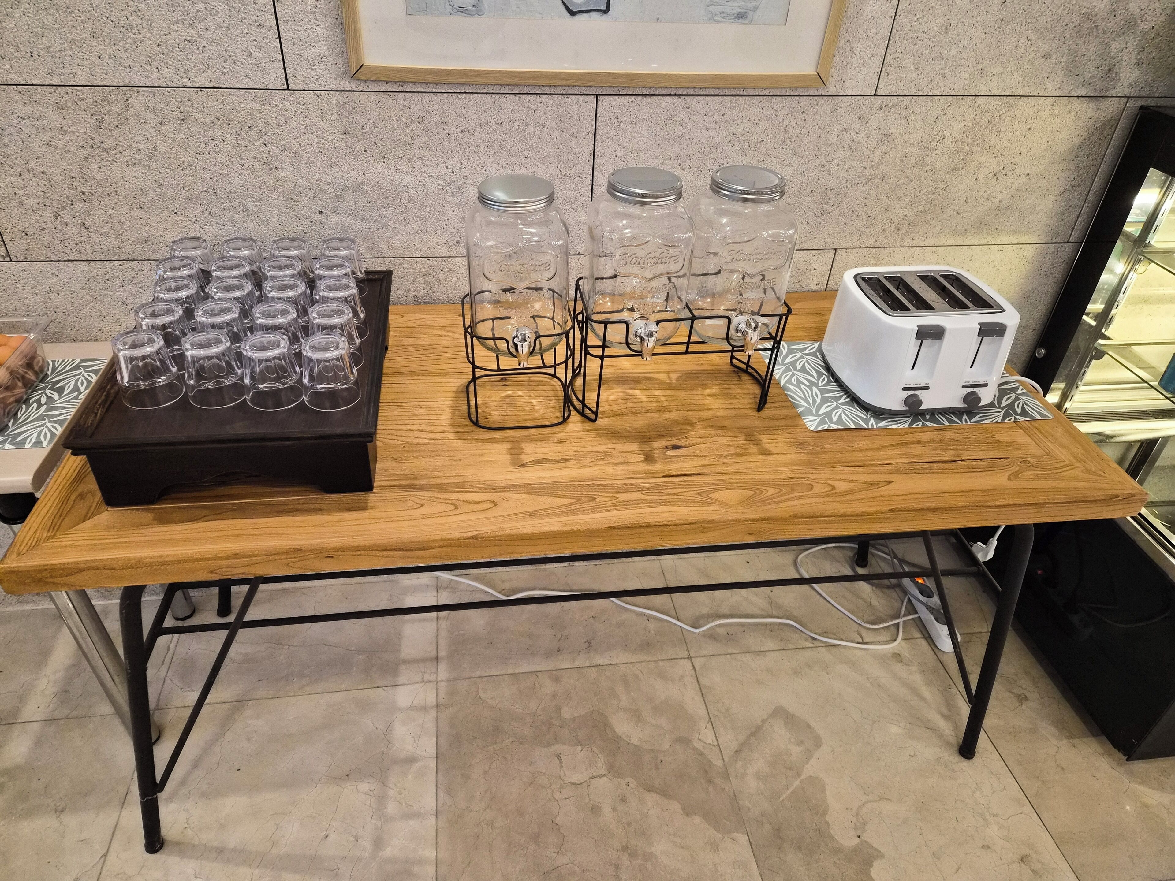 Una mesa de madera con estructura de metal negro, un tostador y frascos de vidrio en una bandeja.