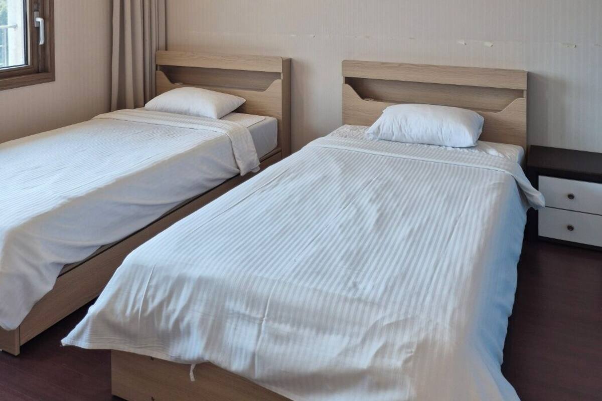 Una habitación de hotel con dos camas individuales, una ventana con cortinas y una mesita de noche con lámpara.