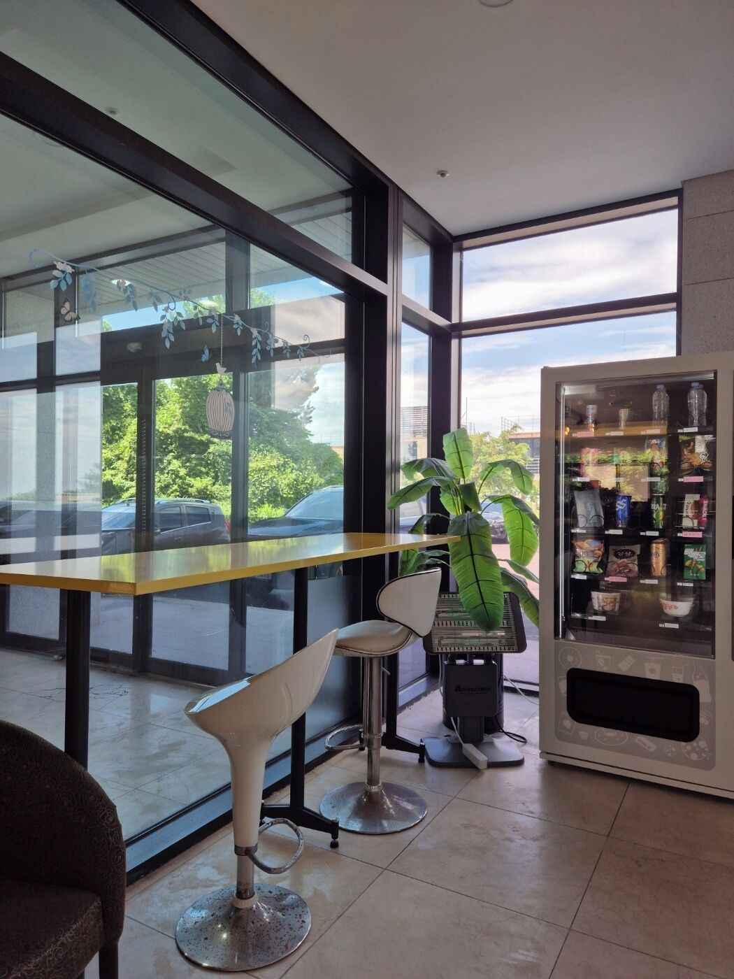 A modern interior with a glass partition, a vending machine, and a view of greenery outside.