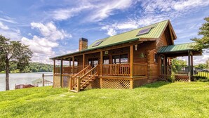 Een houten chalet met een groen dak, een overdekte veranda en een trap naar de ingang.