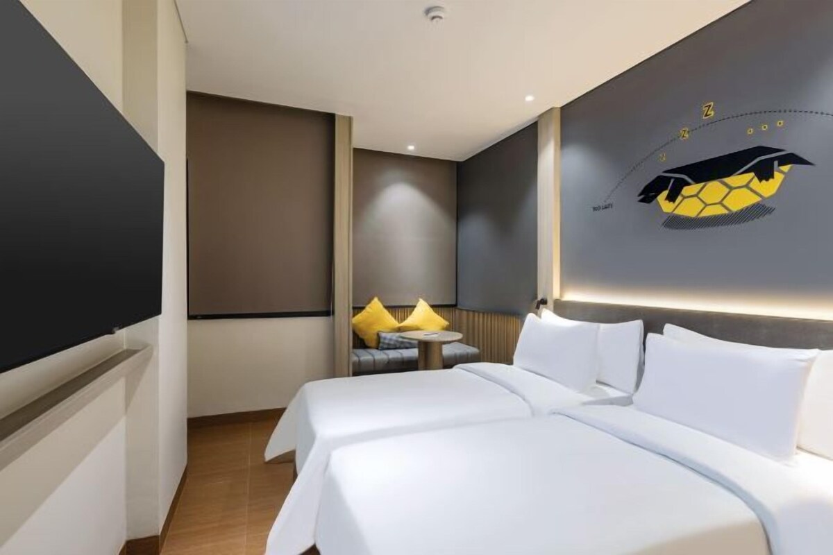 A hotel room with two beds, a sofa, and a wall-mounted TV.