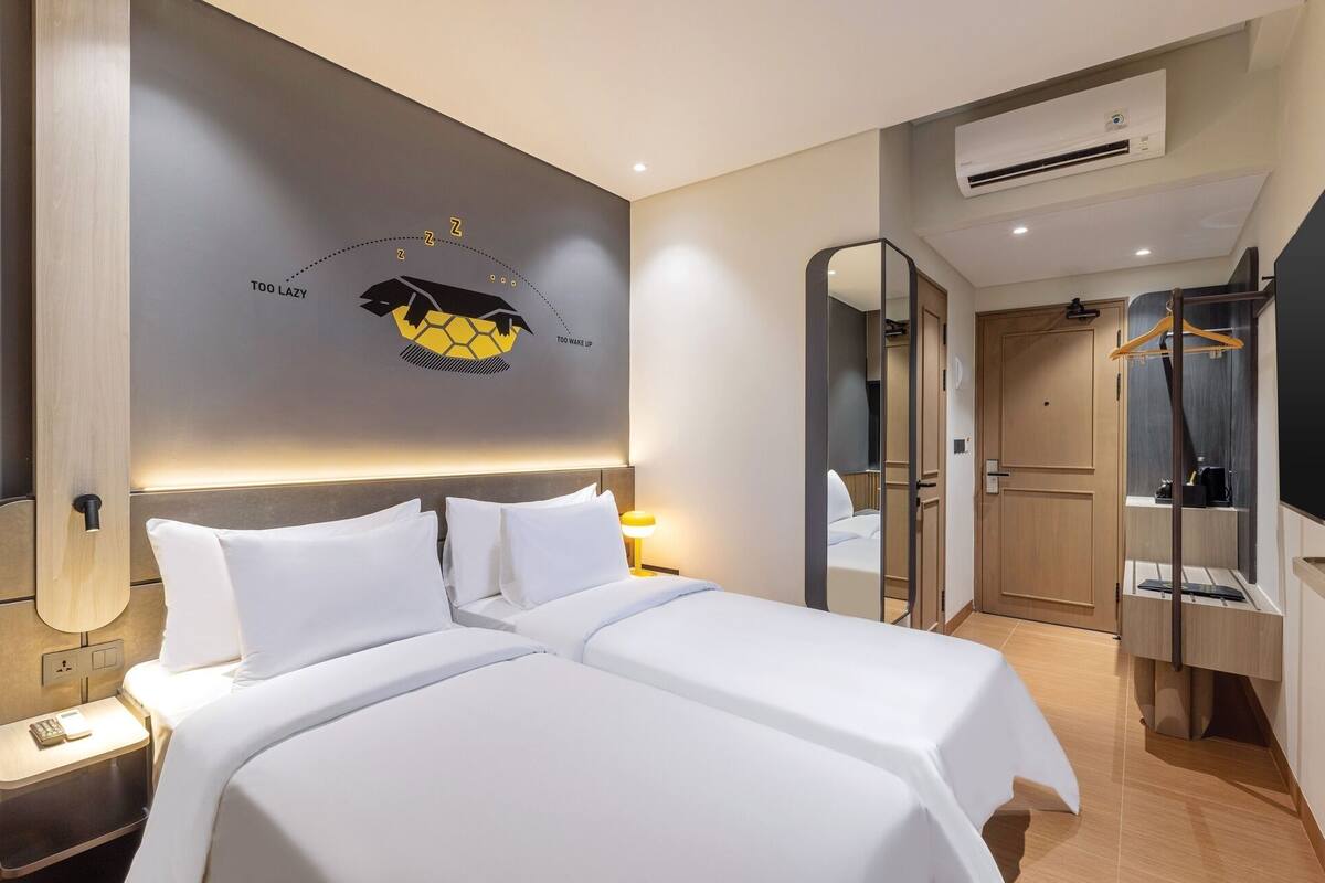 Una habitación de hotel con cama, mesitas de noche, espejo, armario y unidad de aire acondicionado.