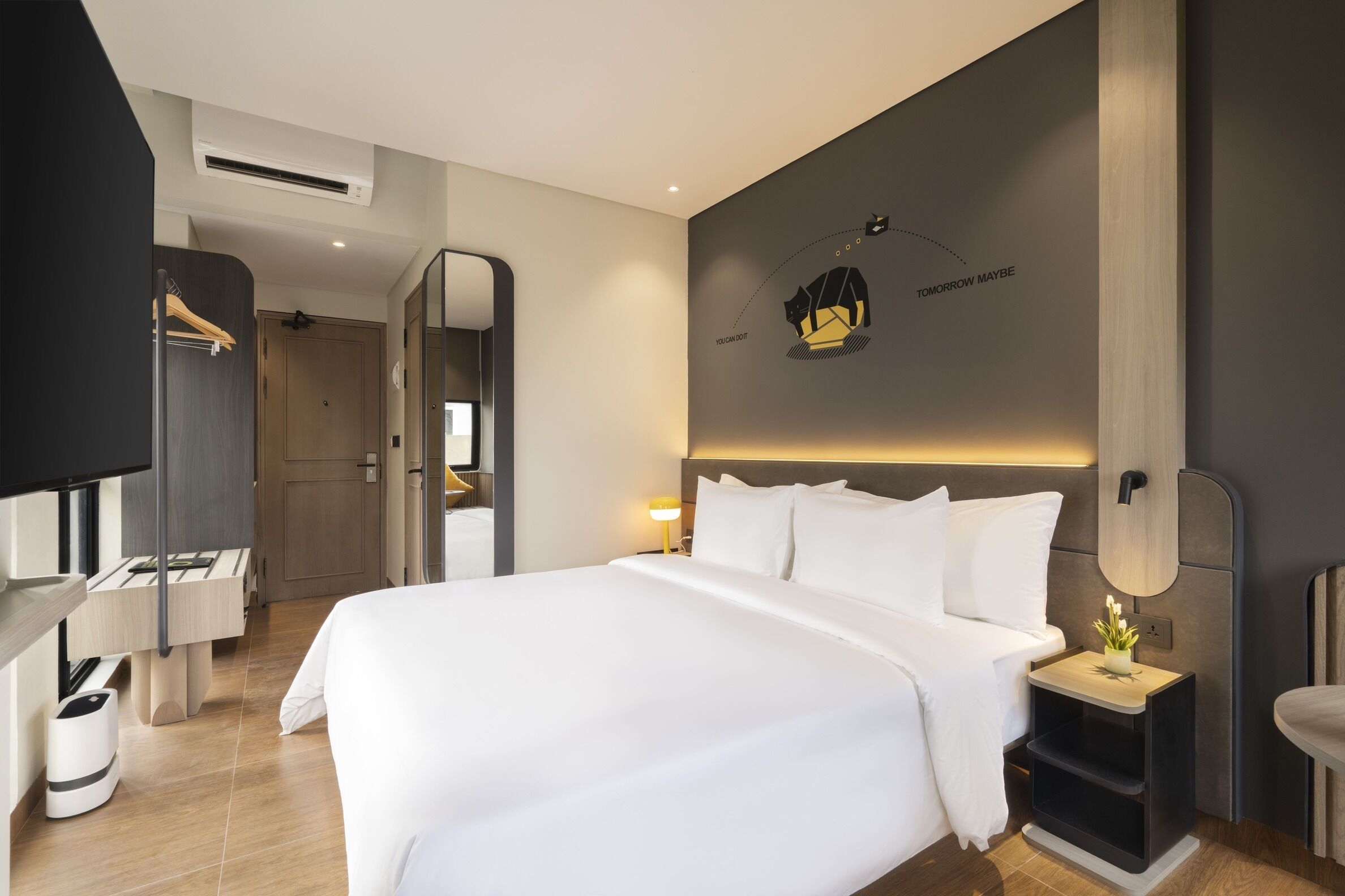 A modern hotel room with a large bed, bedside tables, a mirror, and a wall-mounted artwork.