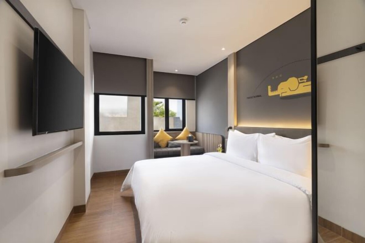Une chambre d’hôtel moderne dotée d’un grand lit, d’un téléviseur à écran plat fixé au mur et d’une fenêtre donnant sur l’extérieur.