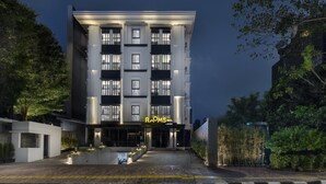 A modern hotel with a prominent 'ROOMS INC.' sign, multiple floors, and a well-lit entrance.