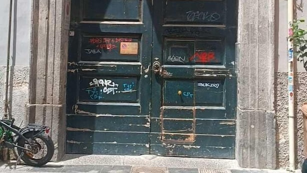 Ein großer, bogenförmiger Eingang mit einem Metallgitter, ein Fahrrad daneben abgestellt und ein Gebäude mit einem Balkon darüber.
