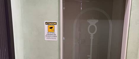 Um corredor com uma porta identificada como "RELAIS CHIAIA" e um aviso de câmera de segurança na parede.