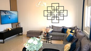 A modern living room with a sectional sofa, a flat-screen TV, a coffee table, and decorative vases. - BH007 - A - Alerine Home (Heraklion)