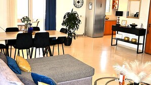 A modern living room with a grey sectional sofa, a round coffee table, and a dining area with a wooden table and chairs. - BH007 - A - Alerine Home (Heraklion)