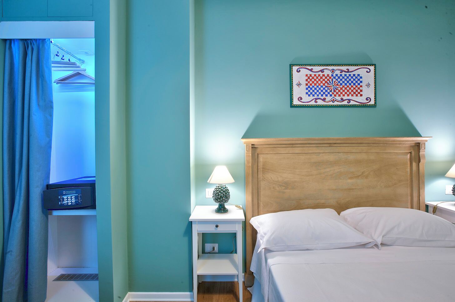 A hotel room with a bed, two bedside tables with lamps, a wall-mounted artwork, and a window with curtains.