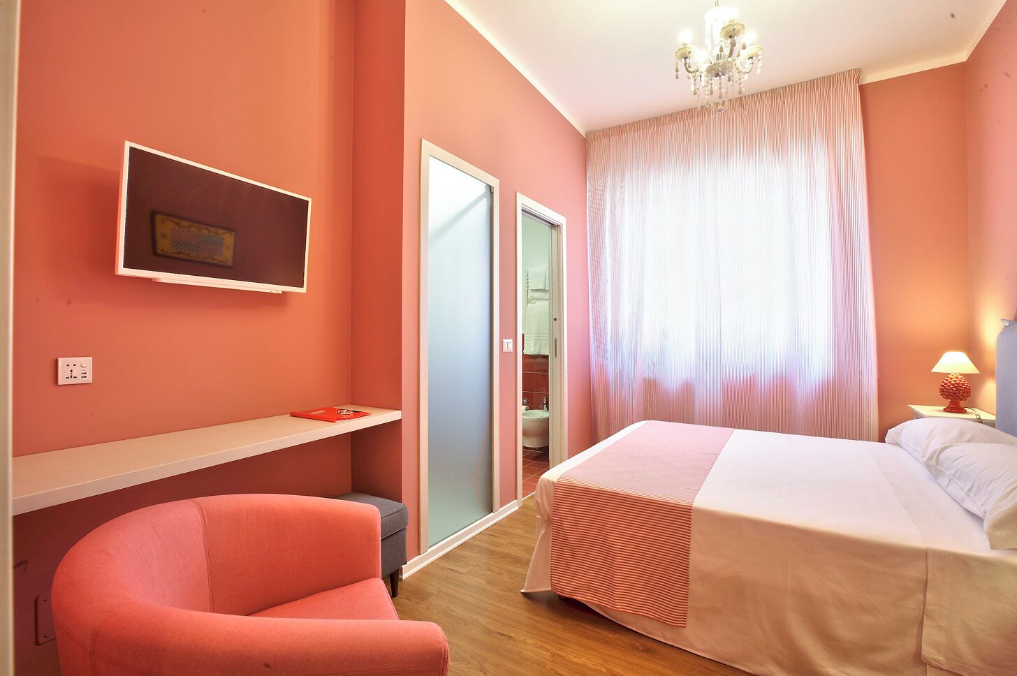 Ein Schlafzimmer mit Bett, Stuhl, Schreibtisch, Spiegel und einer Chandelüster.
