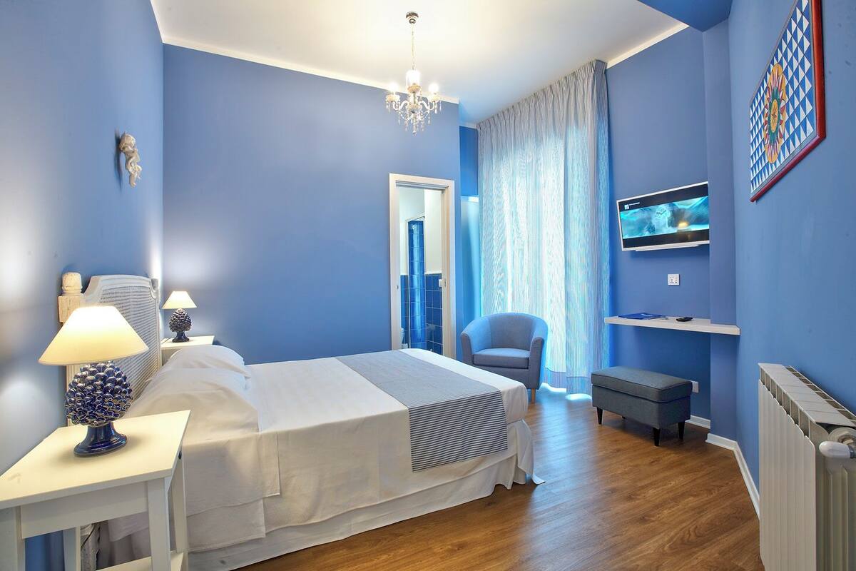 A hotel room with a bed, bedside tables, a chair, a TV, and a radiator.