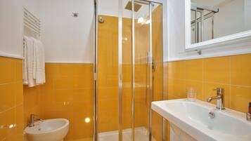 A bathroom with a glass-enclosed shower, a sink, and a bidet.