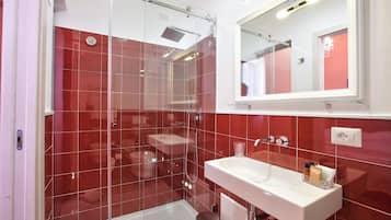 Une salle de bain moderne avec des carreaux rouges, une douche en verre, un lavabo blanc et un miroir au-dessus du lavabo.