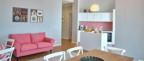 A dining area with a wooden table and white chairs, a pink sofa, and a chandelier.