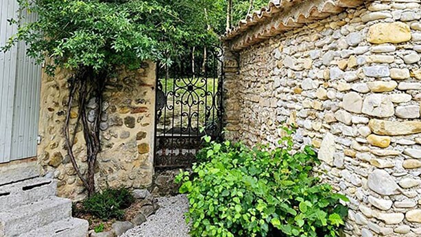 A stone wall with a metal gate, a small garden area with green plants, and a concrete staircase leading up to a door. - Rare product: Top-of-the-range Provencal farmhouse in the heart of the vineyards (Villedieu)
