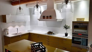 A modern kitchen with wooden cabinets, a central island, pendant lights, and built-in appliances. - Rare product: Top-of-the-range Provencal farmhouse in the heart of the vineyards (Villedieu)