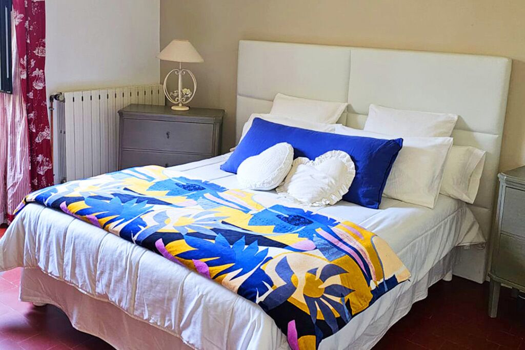 A bed with a colorful bedspread, a white headboard, and a bedside table with a lamp.