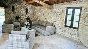 A stone-walled room with wicker furniture, a window, and a wooden ceiling. - Rare product: Top-of-the-range Provencal farmhouse in the heart of the vineyards (Villedieu)